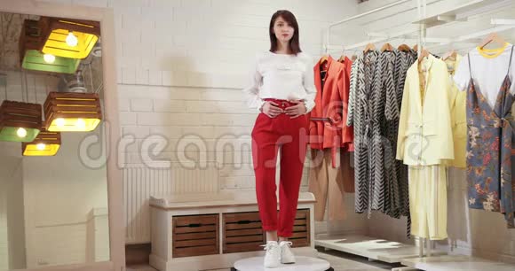 一个美丽的女孩围绕着她的轴心旋转在转盘上展示服装模型穿着大衬衫和红裤的模特视频的预览图