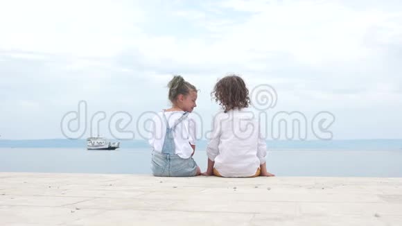 柯利的孩子们几个十几岁的孩子手牵着手坐在海边的码头上看着一艘漂浮的船视频的预览图