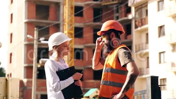 微笑的年轻建筑师或工程建设者戴着安全帽她的手里拿着文件夹一群建筑工人在视频的预览图
