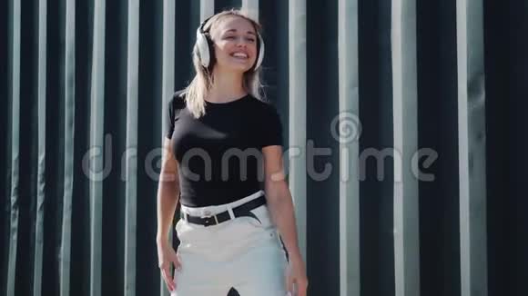 微笑的女孩用耳机听音乐在黑墙背景下跳舞视频的预览图