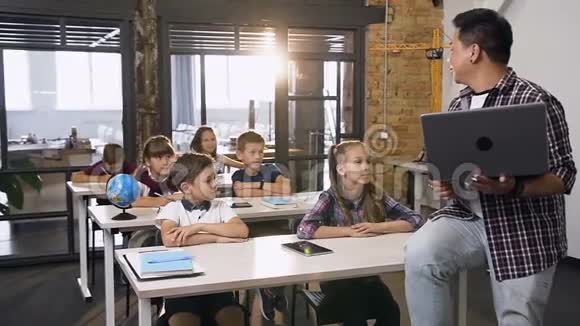 韩国男教师带笔记本电脑为六名小学生上课坐在课桌上的学童视频的预览图