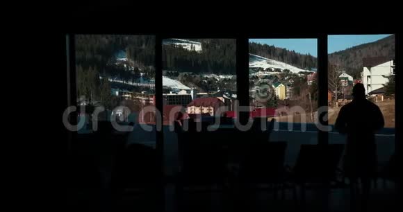 男人走近大的全景窗口欣赏窗外群山的美丽长期射击视频的预览图