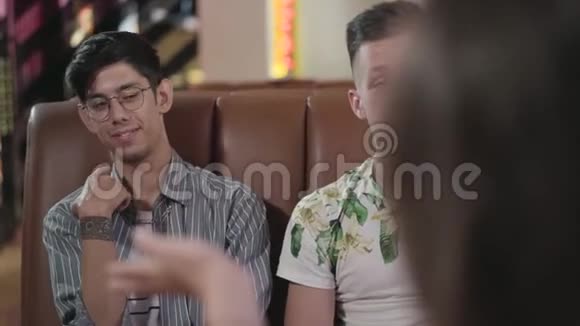 两个男朋友坐在皮革沙发上和餐厅里的女孩说话的肖像快乐青年公司视频的预览图