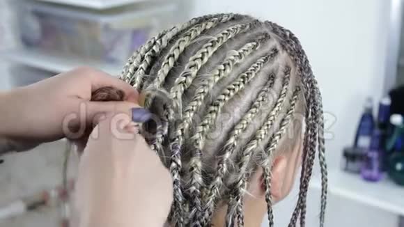 理发师用模糊的背景金发女孩的头上编辫子视频的预览图