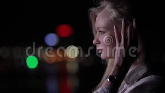 一位美丽的金发女人在夜城摸她的长发视频的预览图
