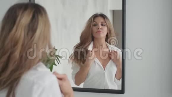 一个迷人的女孩在镜子里崇拜自己的肖像年轻女子直着头发照镜子视频的预览图