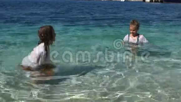 男孩和女孩泼水站在海里的腰部孩子们衣服湿透了快乐的童年视频的预览图