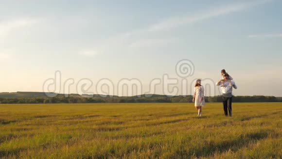 快乐的爸爸抱着一个小女儿在他的怀里和他的妈妈在田里玩父母和孩子一起玩视频的预览图