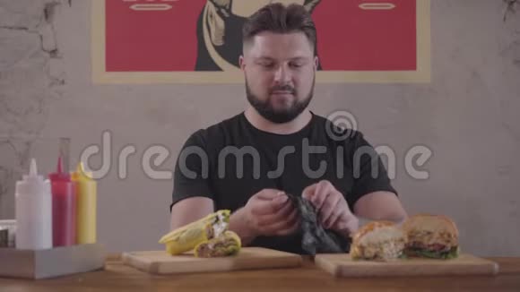 大胡子男人坐在餐桌前的开胃汉堡和沙瓦玛准备吃他穿上了视频的预览图