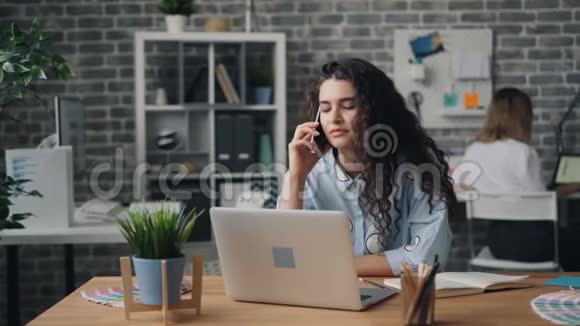 一位年轻女士在办公室用手机说话说着手提电脑视频的预览图