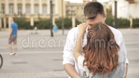 一对深情的年轻夫妇拥抱并分享一个浪漫的吻同时站在城市的一条街上视频的预览图