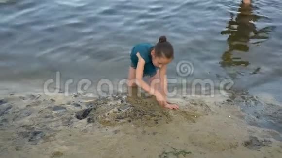 一个小女孩在夕阳西下的水边潮湿的沙子上画了一颗心坐在膝盖上上面的景色视频的预览图
