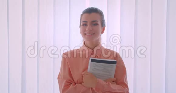 年轻漂亮的女商人举着一本书开心地笑着看着站在摄像机前的特写镜头视频的预览图