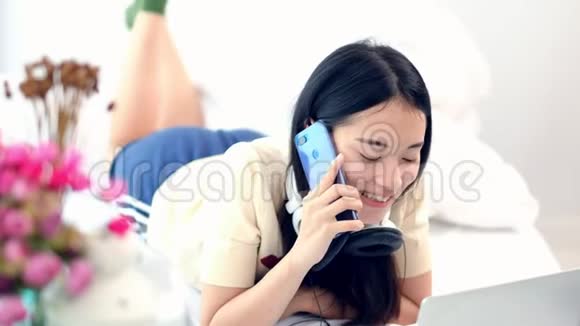 4K年轻的亚洲女人早上躺在舒适的床上用手机说话可爱的少女打电话给她视频的预览图