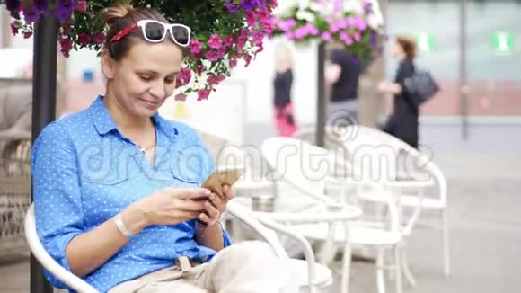年轻女子坐在露台的街头咖啡馆里用她的智能手机视频的预览图