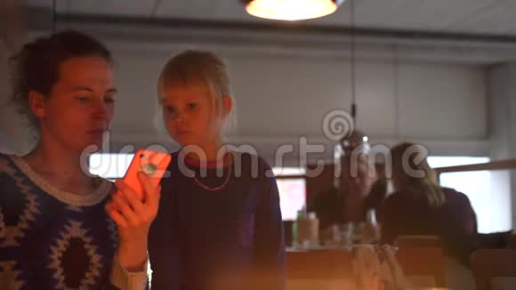 妈妈和女儿在餐馆里使用智能手机视频的预览图