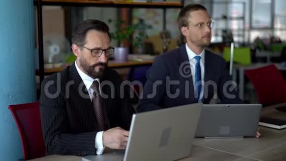 时髦的商人坐在办公室里用笔记本电脑工作视频的预览图