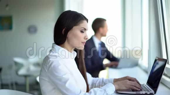 漂亮的女孩正在大光办公室里用笔记本电脑工作视频的预览图