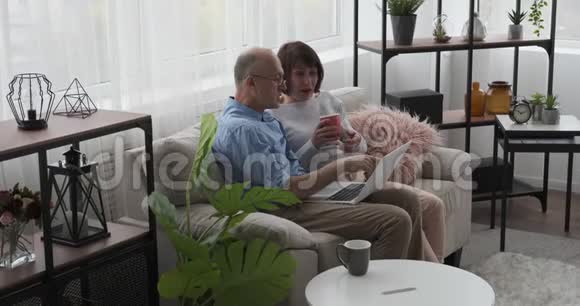 在客厅的沙发上用笔记本电脑放松的老夫妇视频的预览图