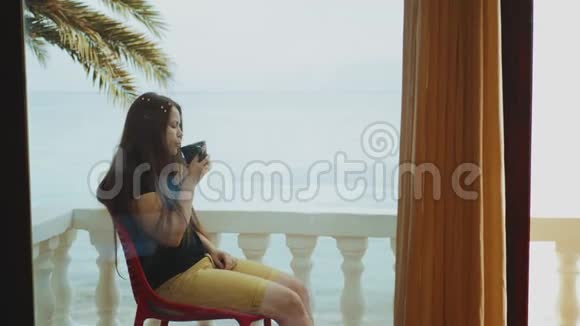 独自一人的女人早上在阳台上喝咖啡或茶从窗户看快速视频视频的预览图