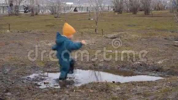 春天穿着防水工作服的快乐男孩穿过水坑视频的预览图