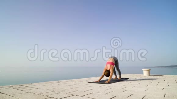 运动女性在石质木板路上做瑜伽背景是大海和天空视频的预览图