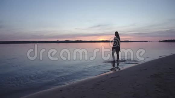 穿着夏装的年轻女子在沙滩上漫步在夕阳的映衬下享受着遥远的生活和自然视频的预览图