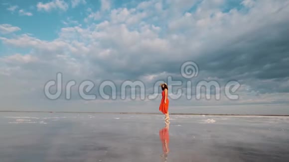 年轻的女旅行者戴着帽子戴着太阳镜沿着一个盐湖走着那里的天空和云彩被反射出来视频的预览图
