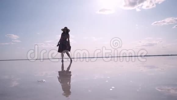 一位年轻女子穿着一件飘舞的连衣裙的剪影沿着一个盐湖奔跑在那里天空被反射视频的预览图