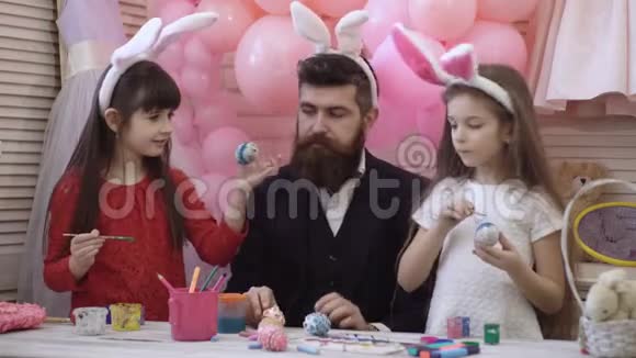 父亲和两个女儿装饰和油漆复活节彩蛋为复活节做准备的幸福家庭可爱的小女孩穿着视频的预览图