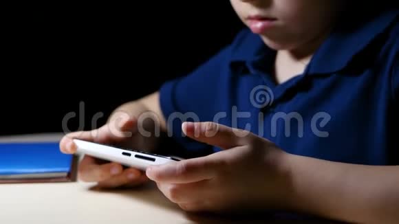 一个孩子晚上在家看漫画用智能手机坐在一张灯点亮的桌子旁特写镜头视频的预览图