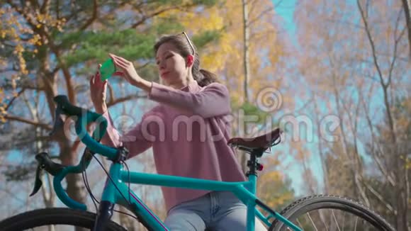 在公园里小女孩拿着一辆固定的齿轮自行车站在手机上拍照视频的预览图