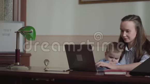 年轻的女人在她的笔记本电脑上打字坐在舒适的椅子上和一个孩子在一起女士停止工作然后视频的预览图