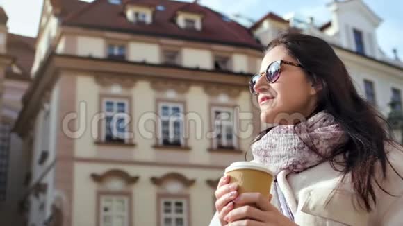 微笑美女喝热饮料纸杯复古建筑背景低角度视频的预览图
