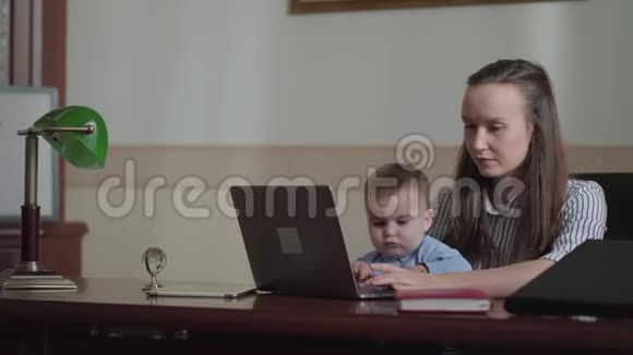 一位严肃的女商人带着婴儿和笔记本电脑在办公室工作视频的预览图