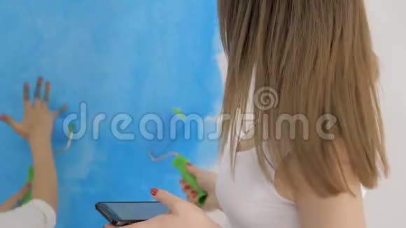 年轻的家庭在母亲查看短信时用滚筒粉刷墙壁视频的预览图