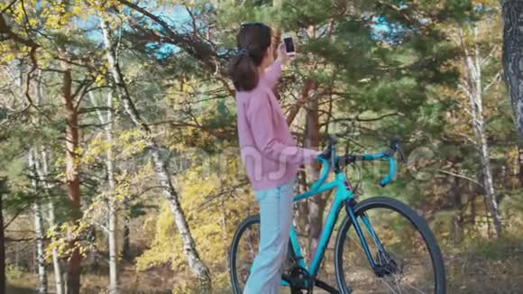在公园里小女孩拿着一辆固定的齿轮自行车站在手机上拍照视频的预览图
