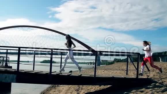 女孩们跑过沙滩上的桥头发飘飘阳光灿烂蓝天视频的预览图
