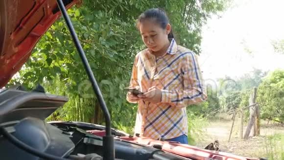 亚洲年轻女子打电话给汽车修理工同时站在路上的断车附近视频的预览图