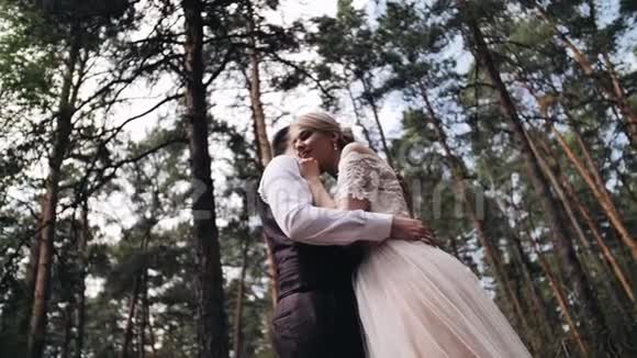 一对相爱的夫妇拥抱在一片美丽的松林里穿着白色裙子的女孩靠在男朋友身上把手放在了她的身上视频的预览图