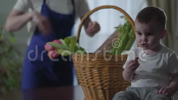 不认识的女孩穿着蓝色围裙一个小男孩坐在桌子上的篮子附近吃东西一个女人拿出食物视频的预览图