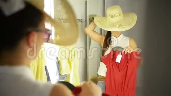 漂亮的女孩在房间背景的镜子附近试衣服戴着滑稽帽子和太阳镜的年轻女人快乐视频的预览图