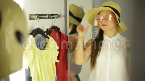 漂亮的女孩试着在化妆室的镜子附近戴太阳镜戴着滑稽帽子的年轻女人快乐购物概念视频的预览图