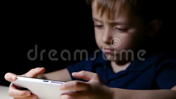 一个孩子晚上在家看卡通片用智能手机坐在一张由灯点亮的桌子旁特写镜头视频的预览图