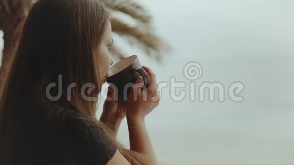 独自一人的女人早上在阳台上喝咖啡或茶从窗户看快速视频视频的预览图