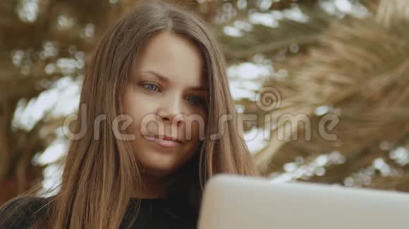 漂亮的女学生或在笔记本电脑上工作的自由职业者坐在阳台上看棕榈和大海速度很快视频的预览图