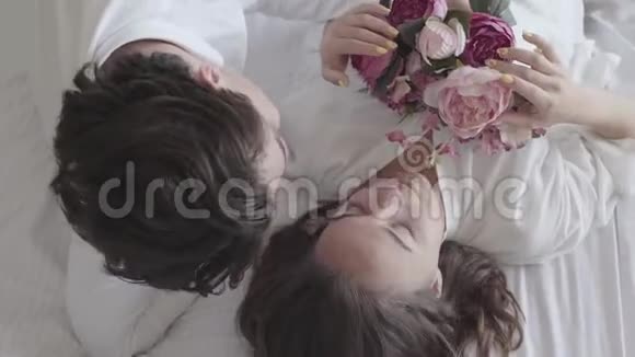 头顶拍摄幸福的年轻夫妇躺在床上说话女人抱着花束微笑的特写投标关系视频的预览图