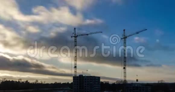 在夕阳的照耀下在多层建筑工地上工作的塔式起重机剪影的时间流逝视频的预览图