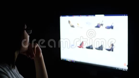 晚上一个带眼镜的黑发女人看着电脑屏幕通过网上扫描鞋子的购买情况视频的预览图