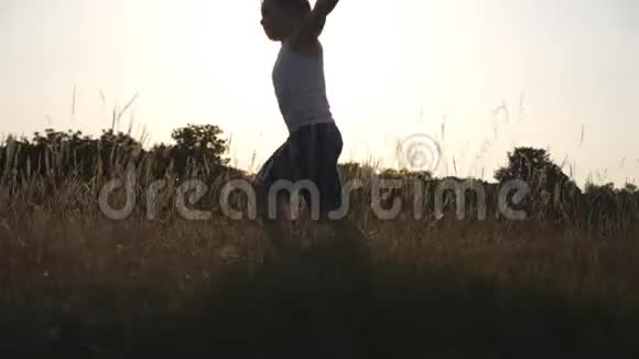 小男孩举起双手像飞机在草地上奔跑日落时分快乐的孩子在草坪上慢跑视频的预览图